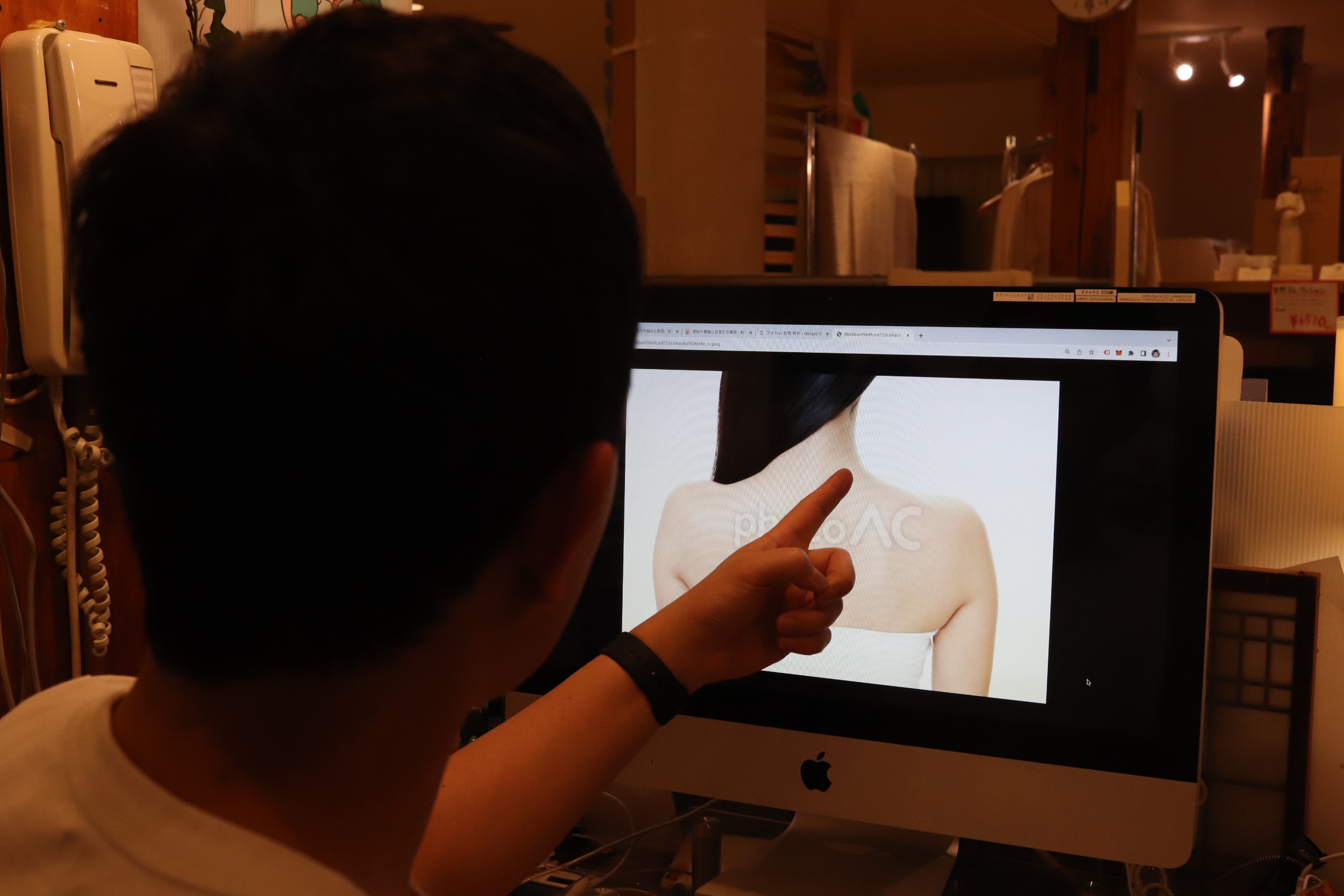 体の細い女性の背中向きの写真をパソコンに表示させ肩を指差す姿
