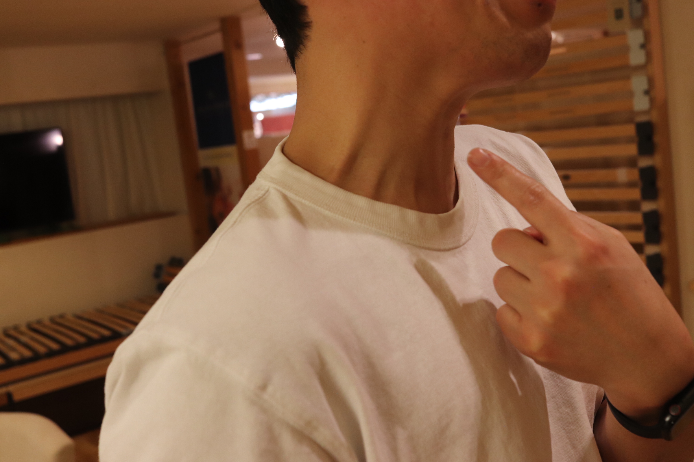 立った姿勢で肩と腕を力ませ首や食いしばりを指差す写真